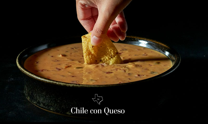 Picture of a hand dipping a chip into queso